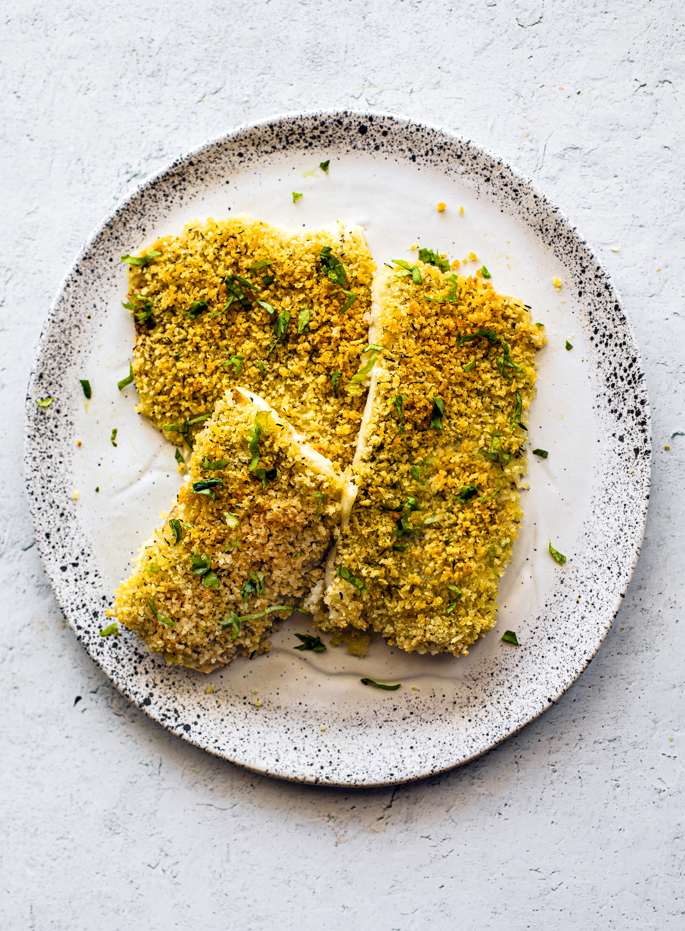 Crispy golden baked flounder on a white speckled serving plate, garnished with fresh parsley.