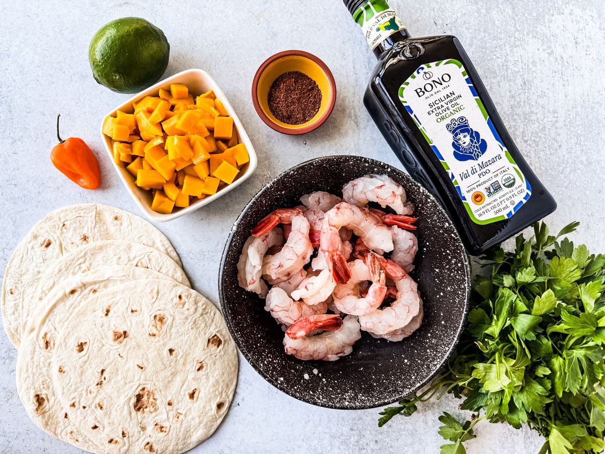 Ingredients for spicy shrimp tacos with mango salsa on a light stone background.