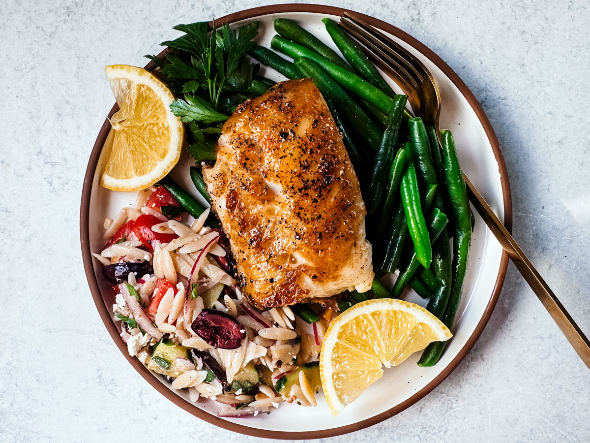 Pan-seared Chilean sea bass fillet on a bed of pasta salad and green beans.