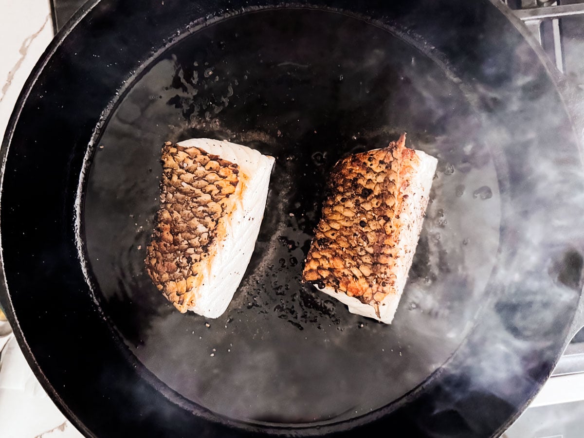 Chilean sea bass fillets being pan seared in a cast iron skillet.