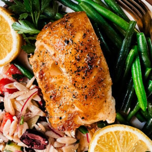 pan-seared chilean sea bass on a plate with green beans and pasta salad.