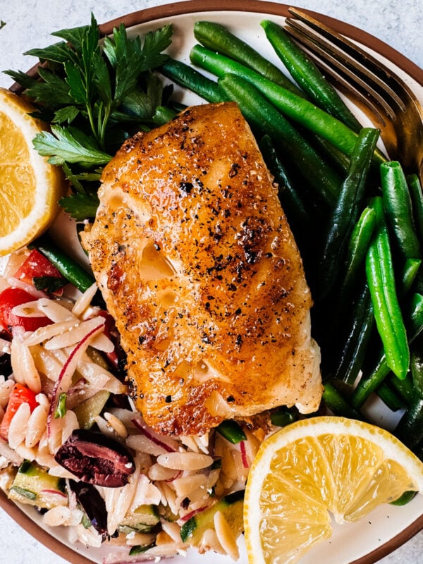 pan-seared chilean sea bass on a plate with green beans and pasta salad.