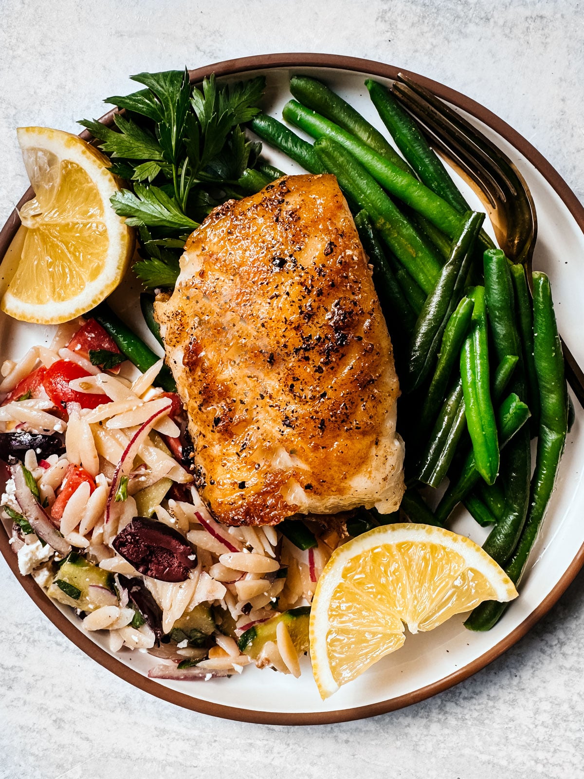 Pan-seared Chilean sea bass fillet on a bed of pasta salad and green beans.