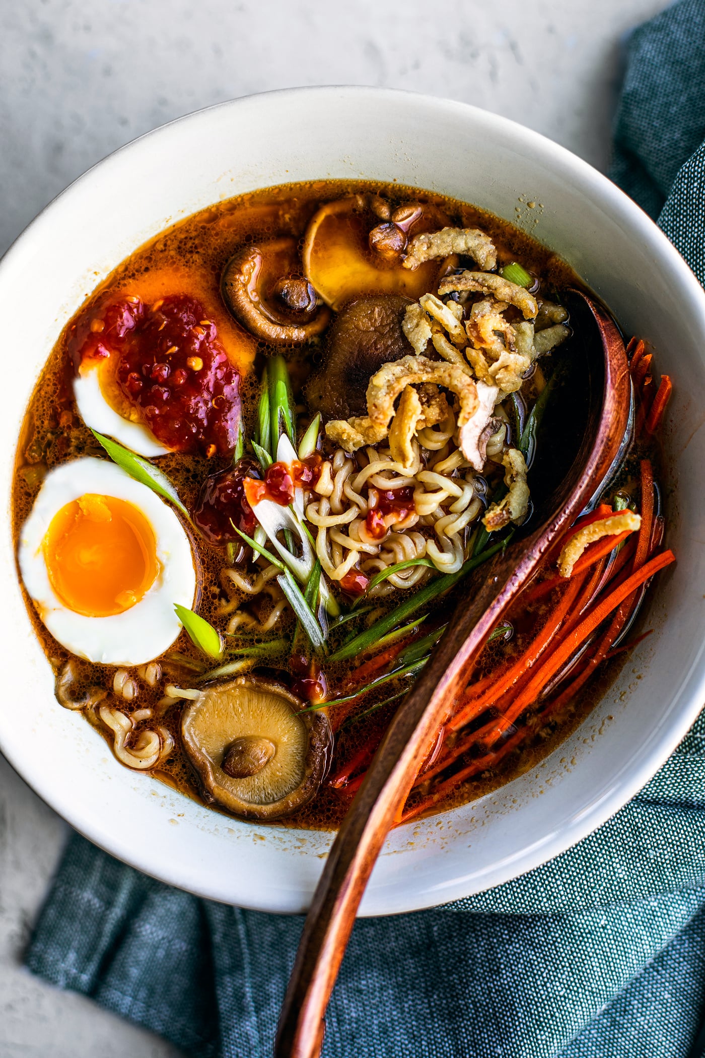 Bowl of miso ramen with soft-boiled egg in it, topped with mushrooms, scallions, and chili sauce.