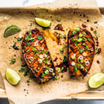 Baking sheet covered in parchment with roasted sweet potato halves smothered in spices and honey, and garnished with scallions.