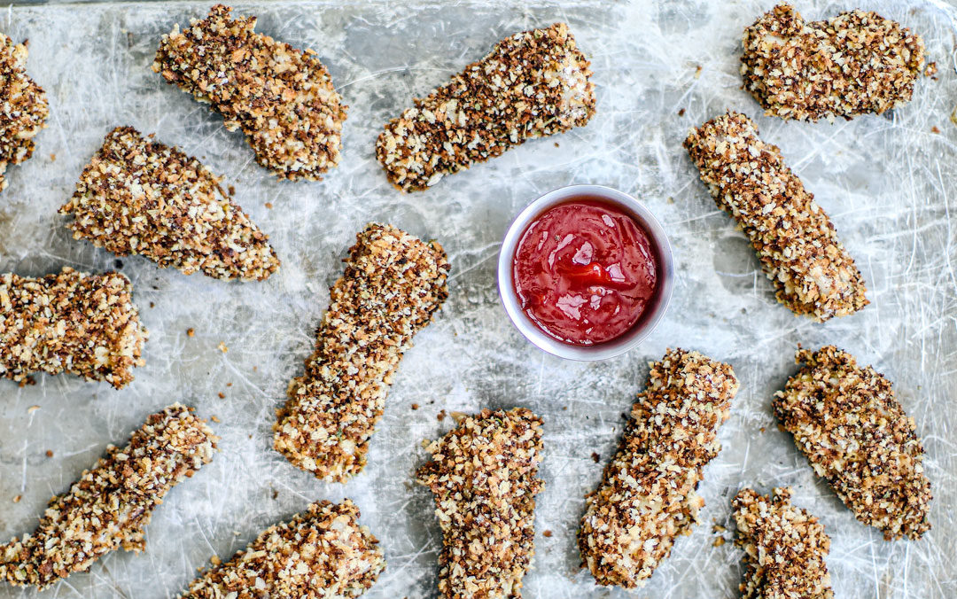 Homemade crispy fish sticks spread out on a baking sheet.