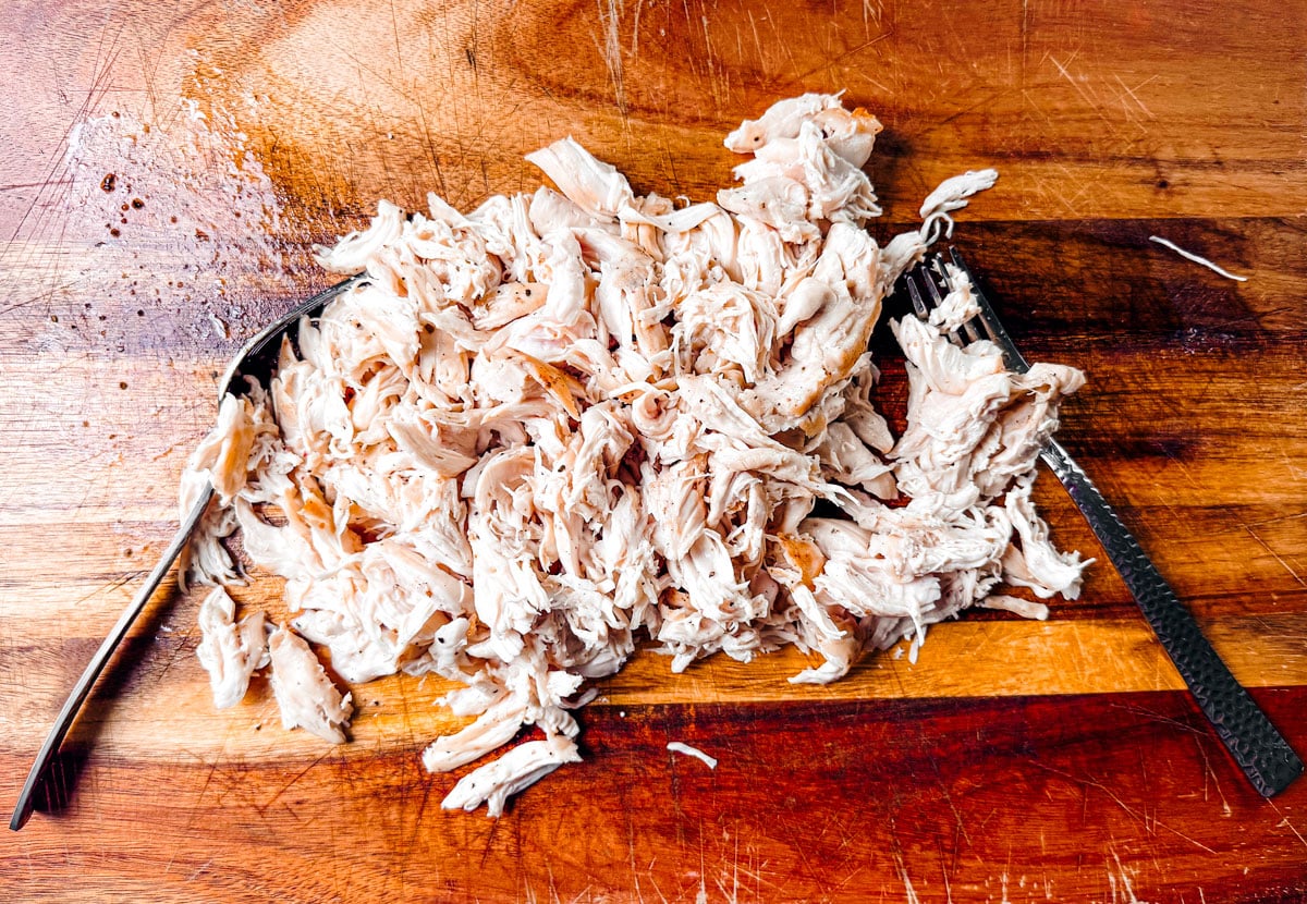 Shredded chicken on a cutting board with two forks.