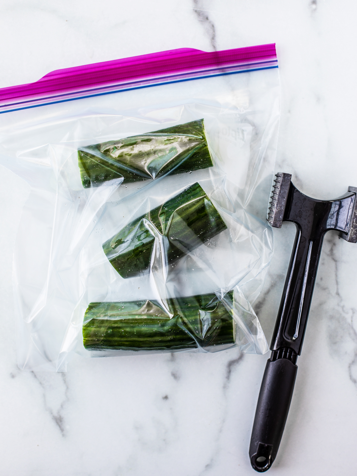 Three cucumber pieces in a freezer bag next to a meat mallet.