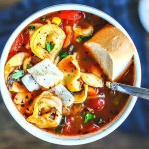 Close up of bowl of vegetable and tortellini soup with bread.