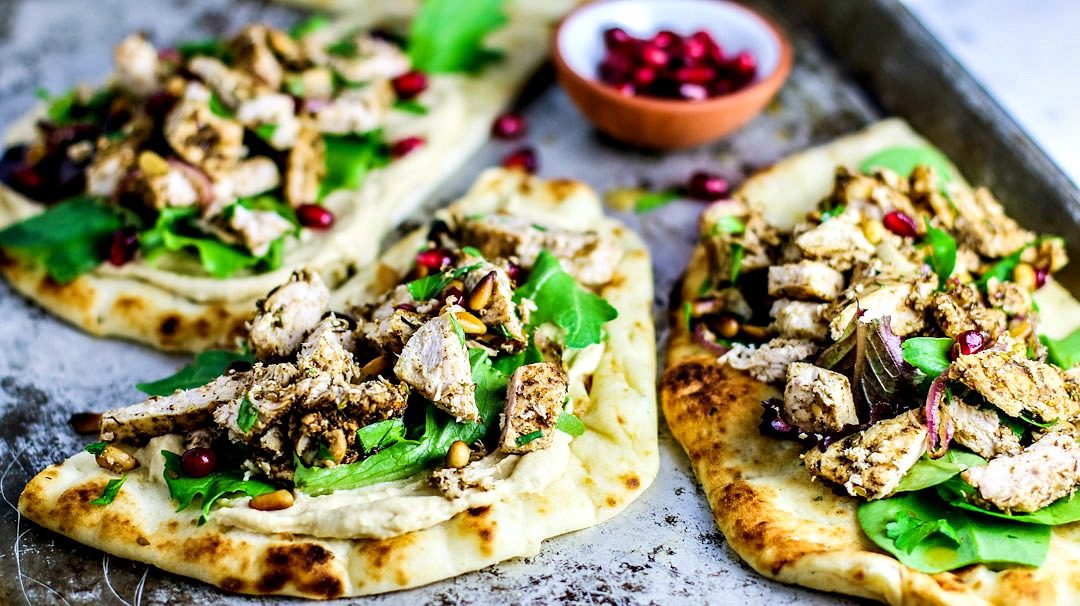 Naan breads topped with hummus, chicken, and greens.