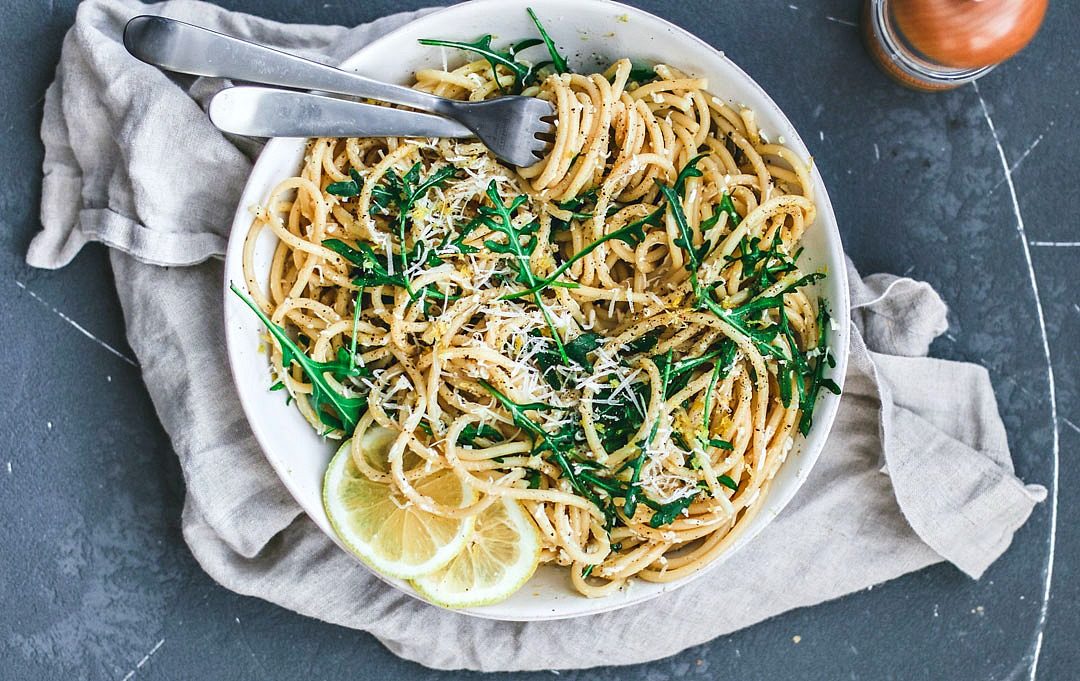 Pasta al Limone piled in a bowl with arugula, whirled around a fork.