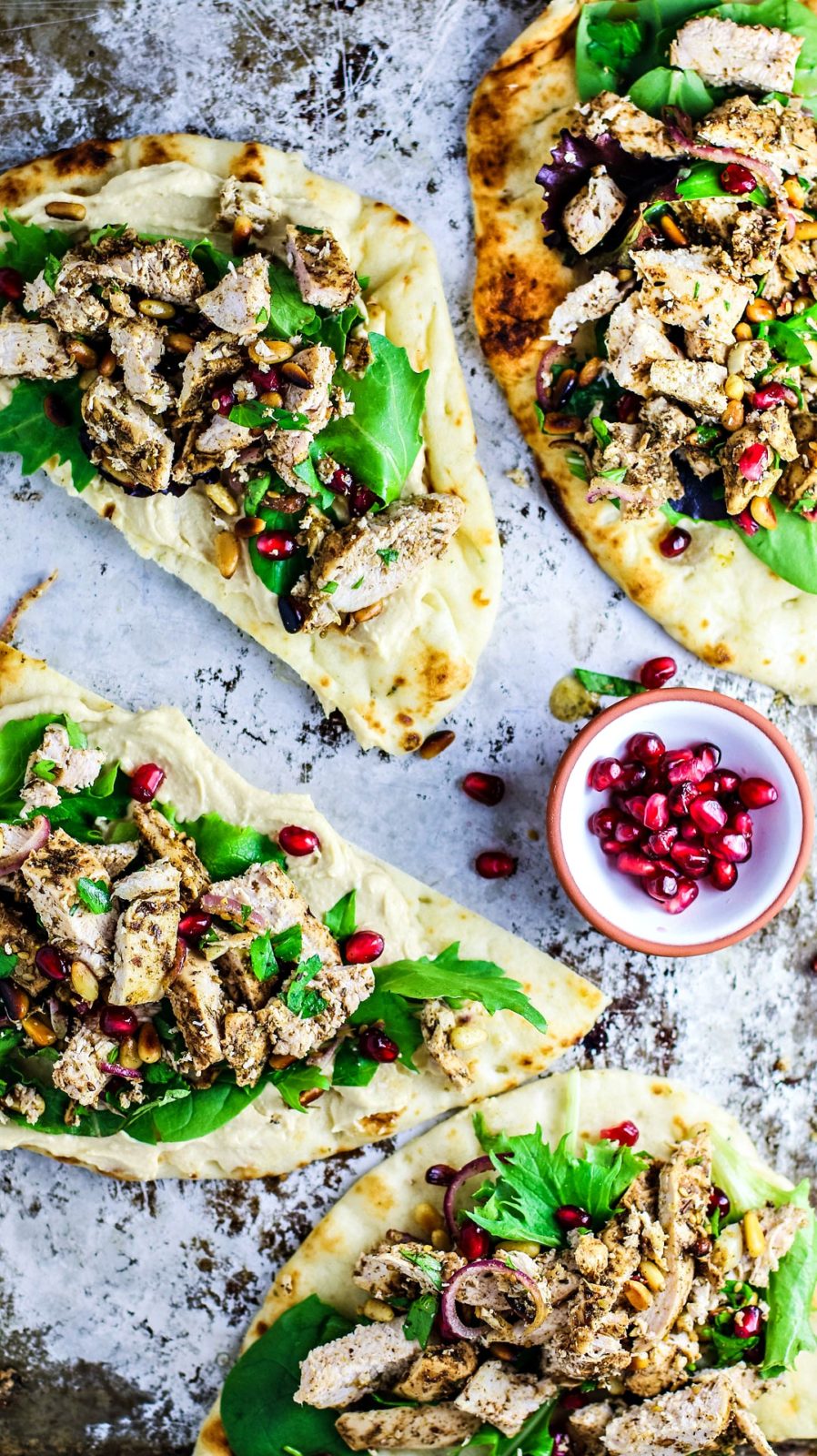 Naan breads topped with hummus, chicken, and greens.