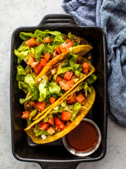 Small black cast iron pan holding tacos topped with tomatoes and lettuce.