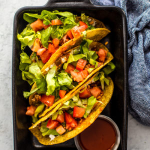Small black cast iron pan holding tacos topped with tomatoes and lettuce.