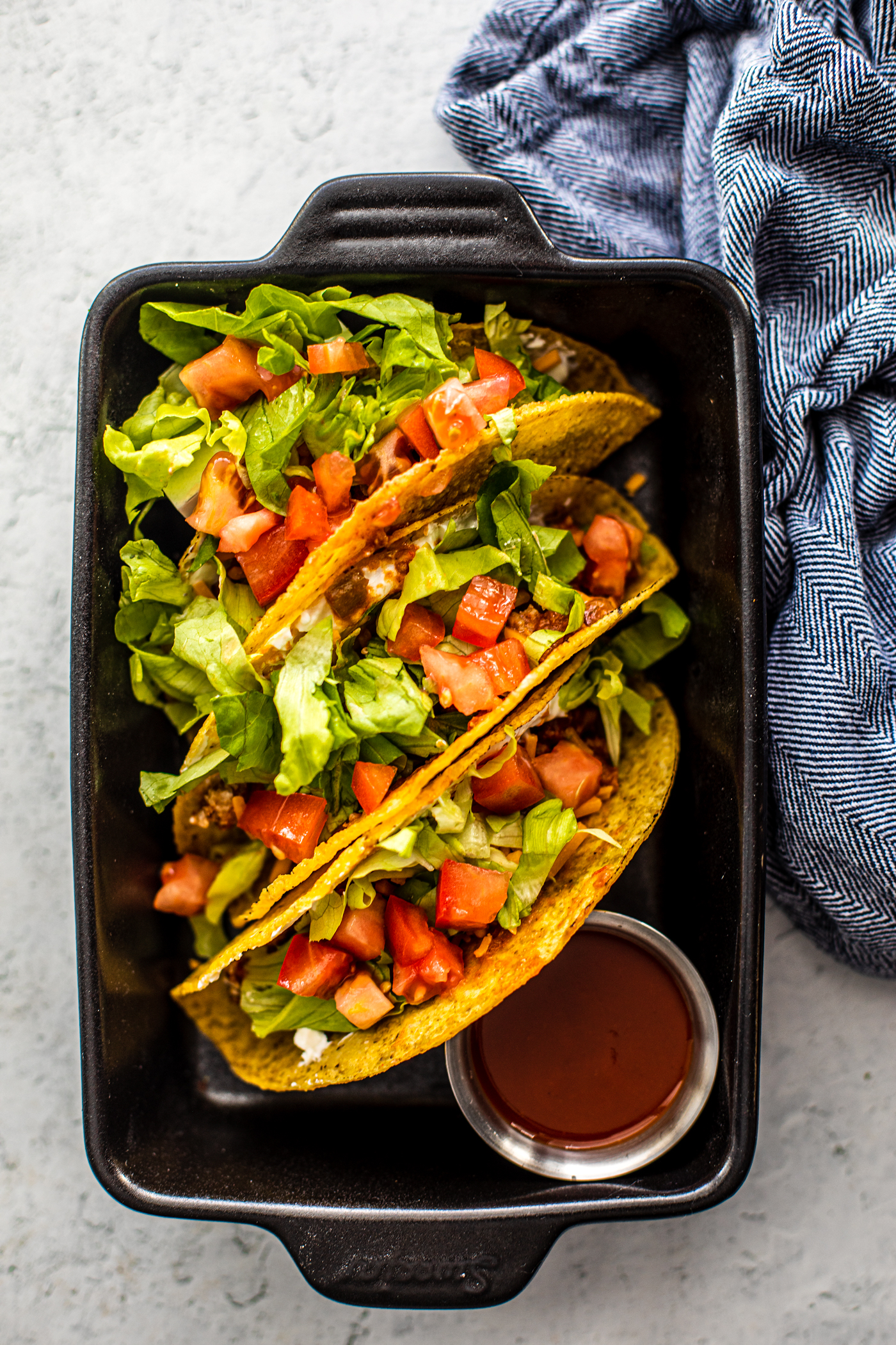 Small black cast iron pan holding tacos topped with tomatoes and lettuce.