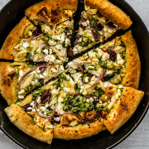 Skillet with chicken pesto pizza cut into slices.