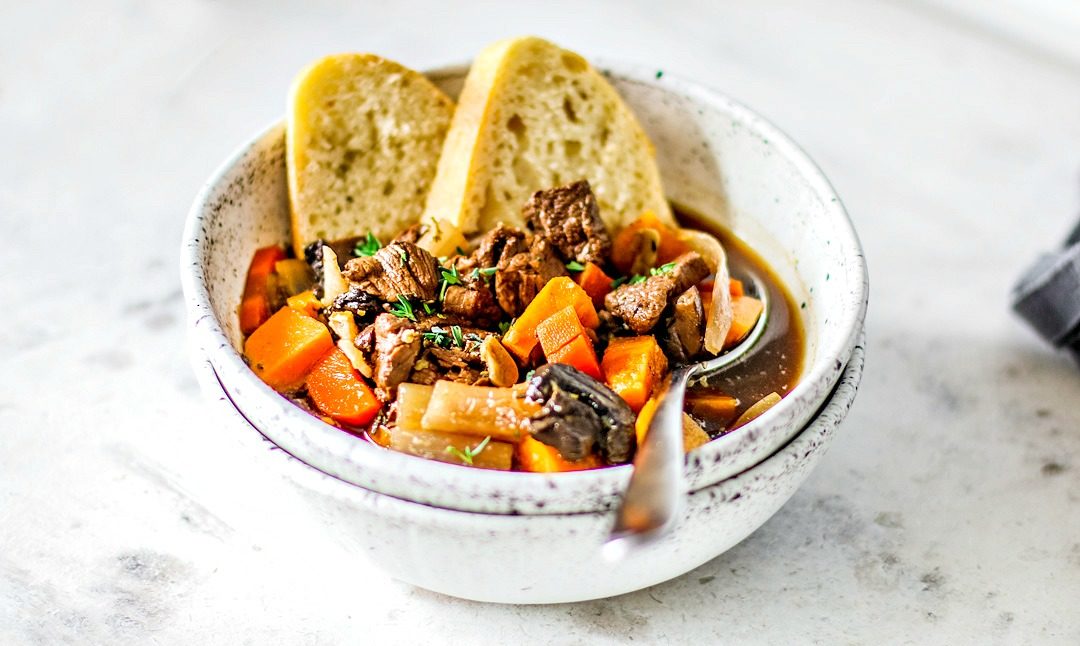 Close up of bowl of beef stew with hunks of crusty bread in it.