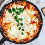Skillet full of bubbling cheesy lasagna garnished with fresh basil.