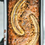 Hands holding up rustic banana bread in bread pan.