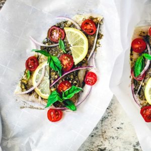 Flounder fillets sitting on parchment paper topped with bright ingredients.