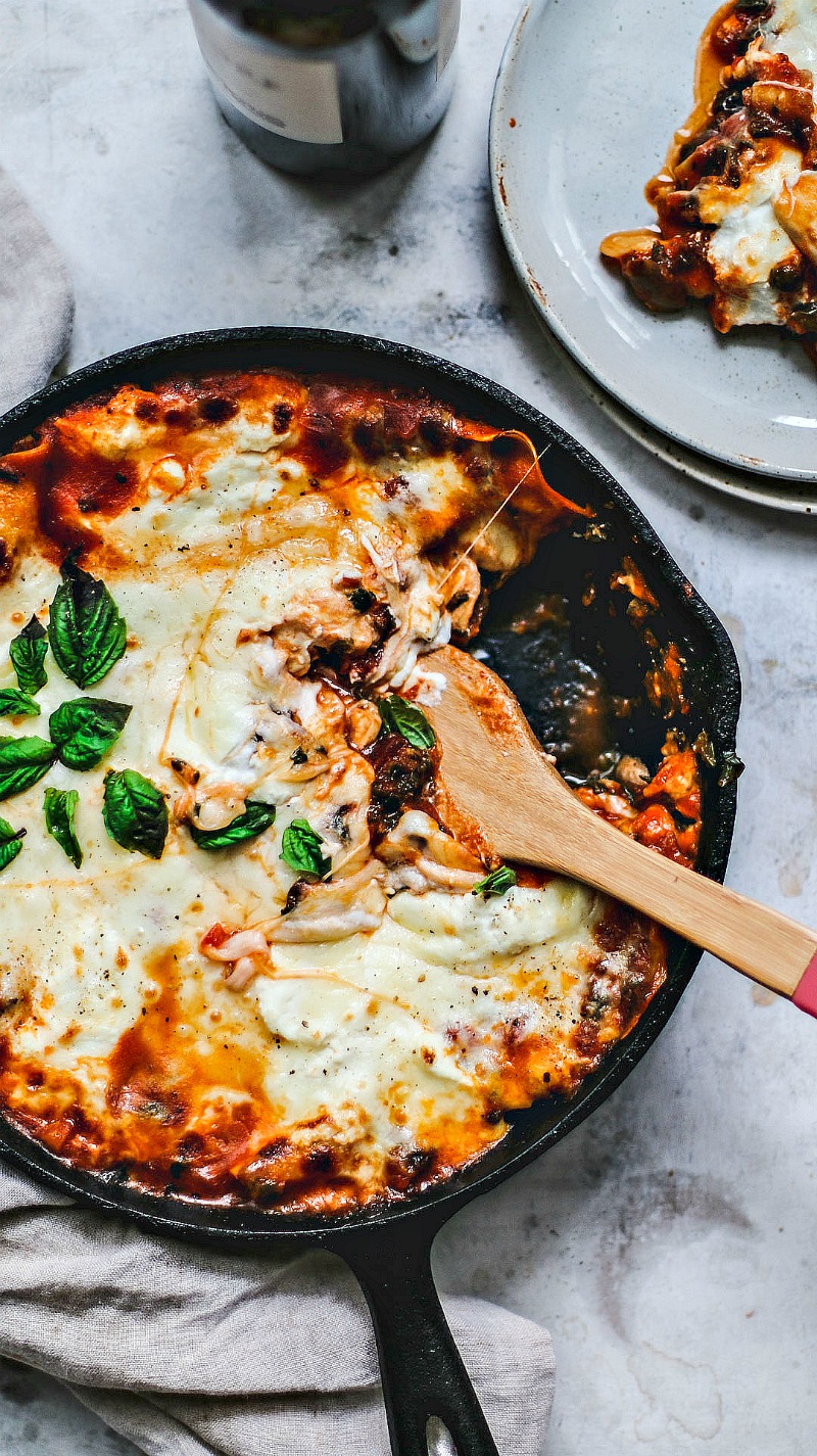 Skillet of lasagna with a portion spooned out.