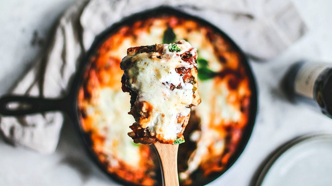 Close up of cheesy lasagna being scooped up by spatula.