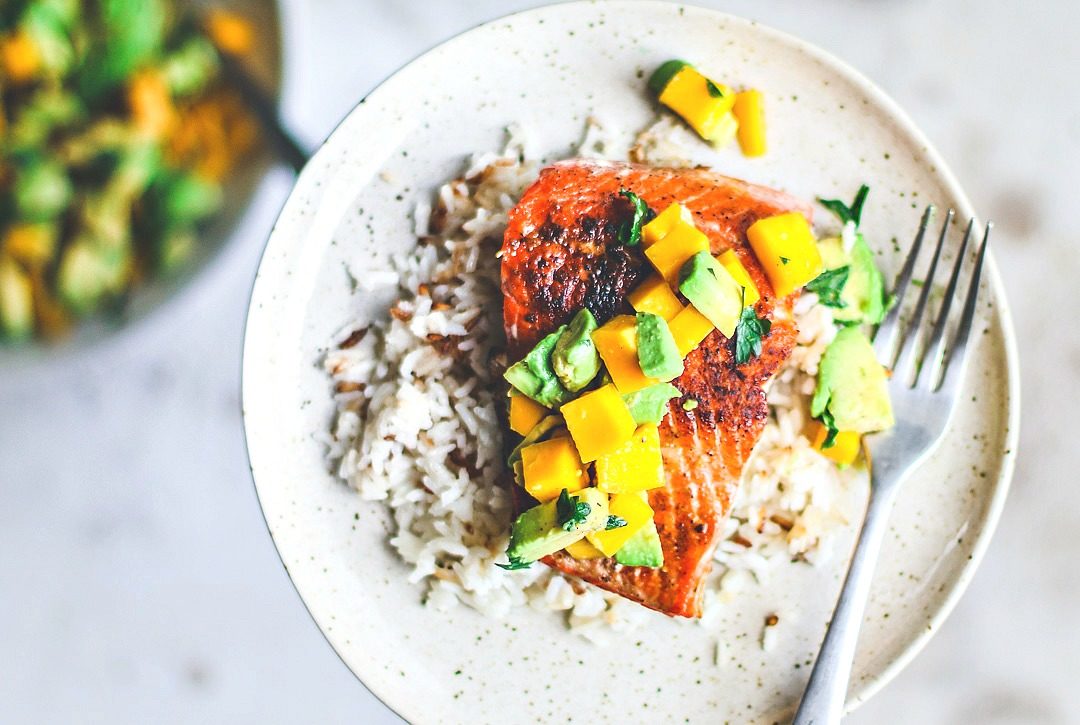 Pan-Seared Salmon on plate over rice and topped with mango and avocado salsa.
