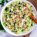 Bowl of lemon and orzo salad with fresh herbs in the background.
