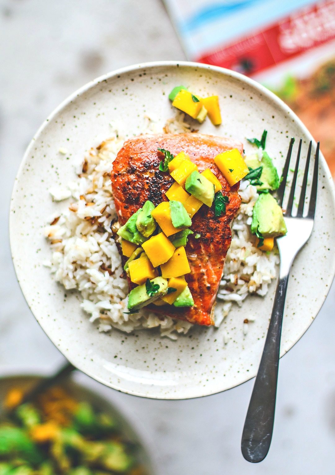 Close up of pan-seared salmon on plate over rice and topped with mango and avocado salsa.