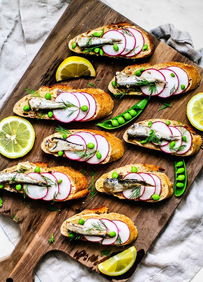 Colorful canapés topped with radishes, peas, sardines, and dill.