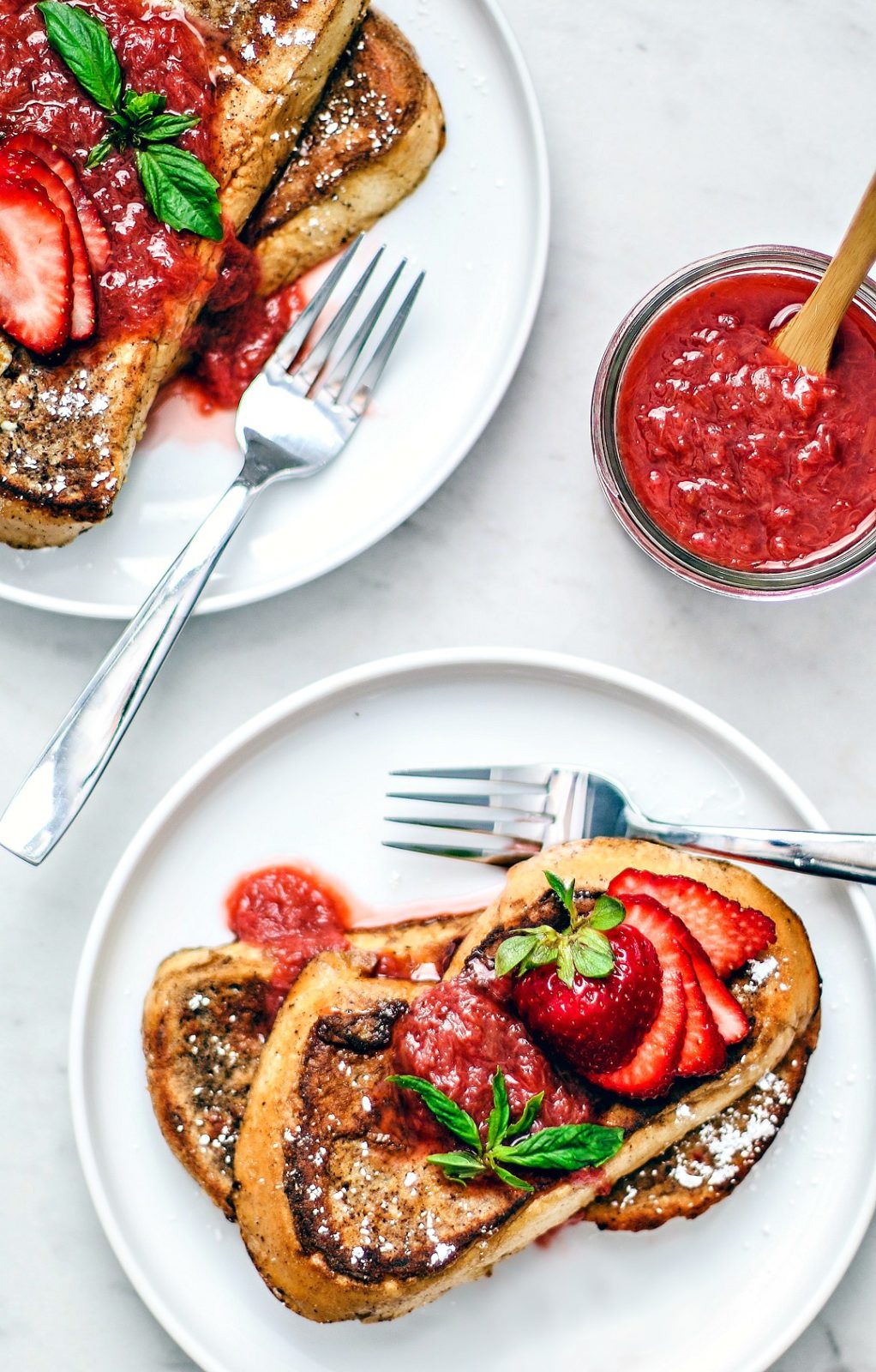 Plated French toast smothered with compote and fresh strawberries.