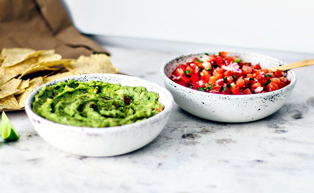 Bowls full of salsa and guacamole with a handful of chips.