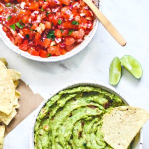 Bowls full of salsa and guacamole with a handful of chips.