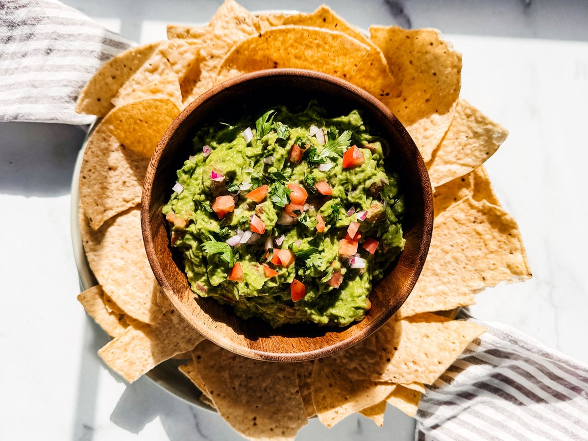 Serving bowl of chunky guacamole surrounded by tortilla chips.