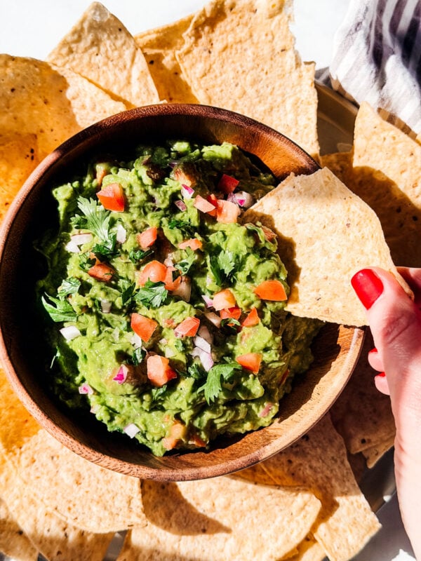 Hand dipping tortilla chip into chunky guacamole.