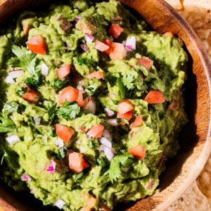 Close up of chunky guacamole with tomatoes, onion, and cilantro as garnish.