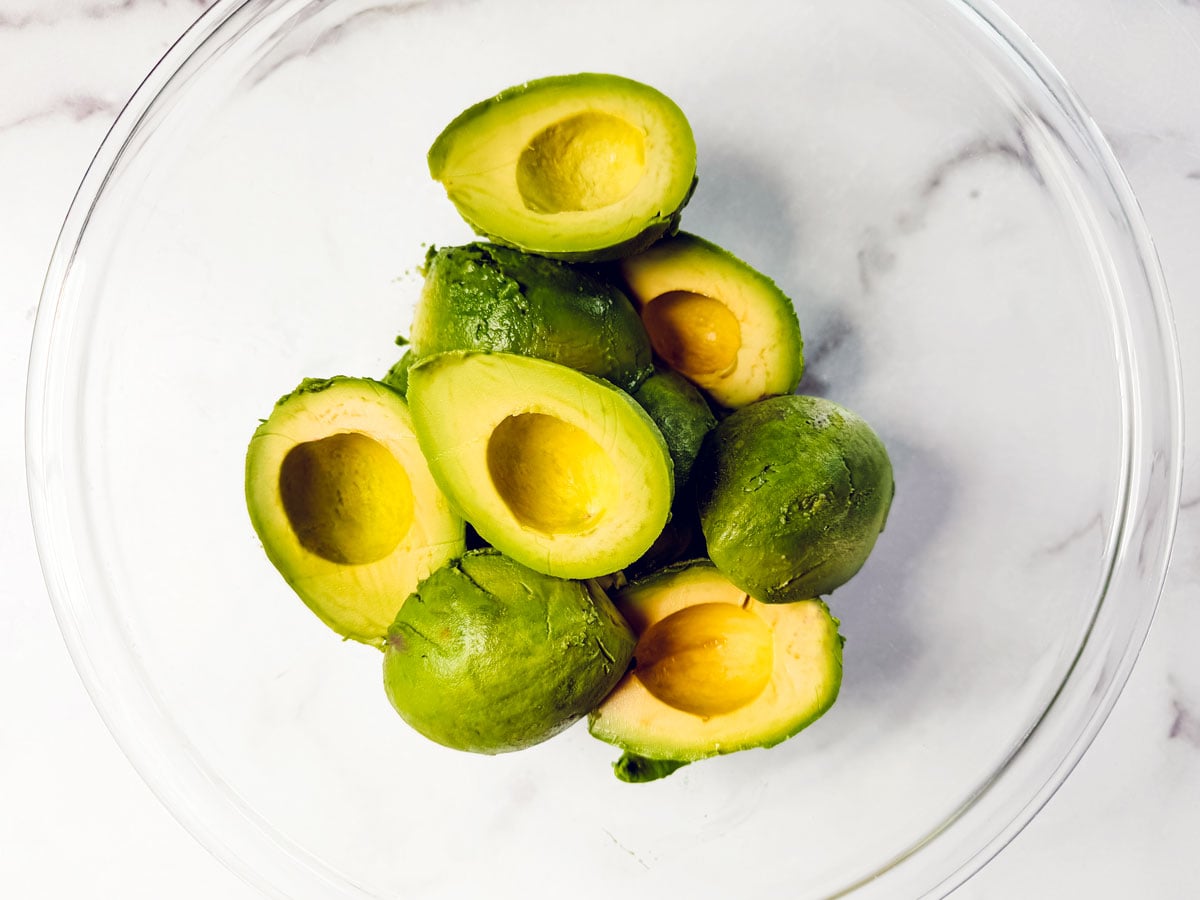 Peeled avocados in glass mixing bowl. 