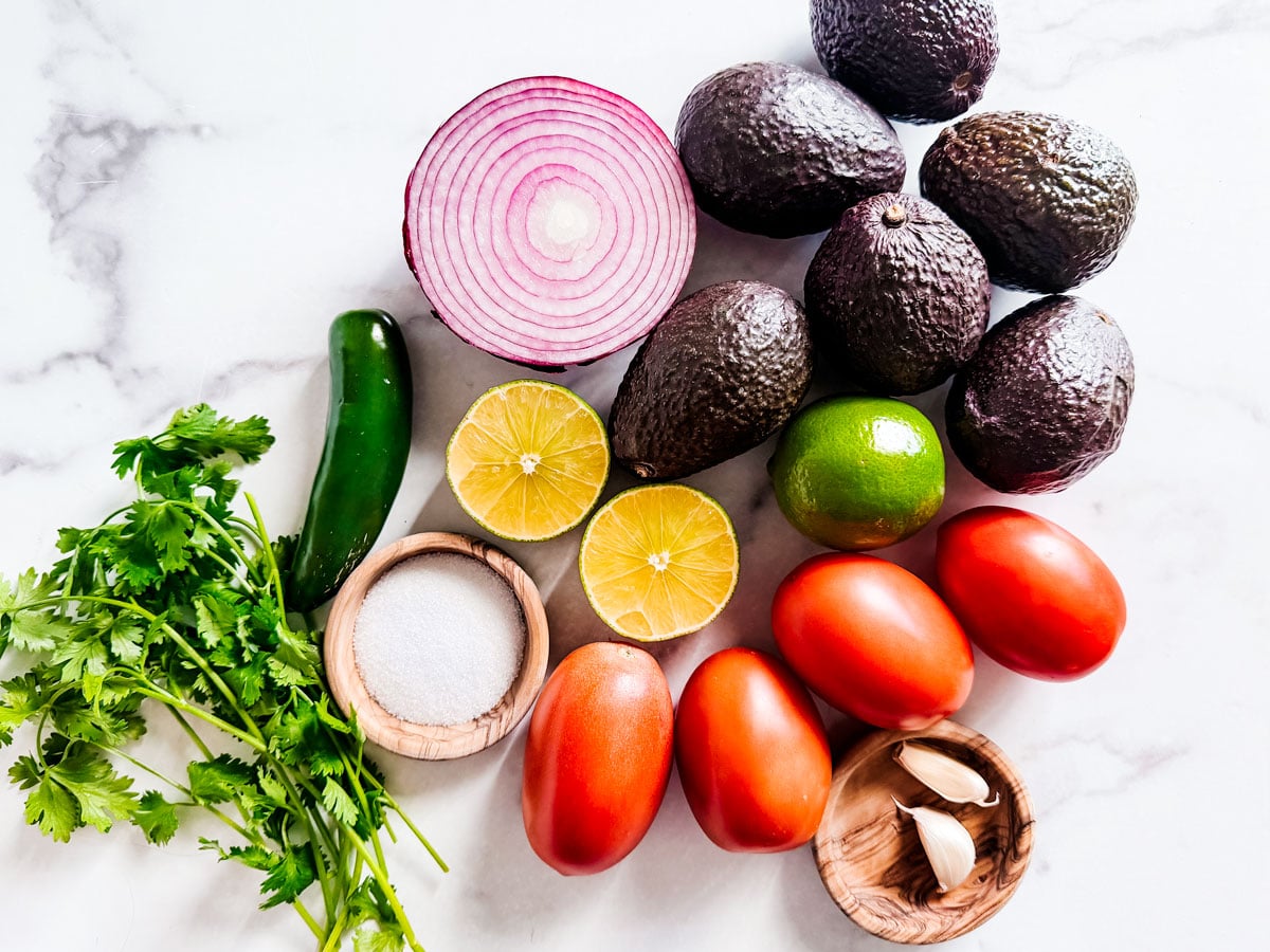 Ingredients for chunky guacamole on white marble background.