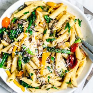A big colorful serving bowl full of pasta and vegetables.
