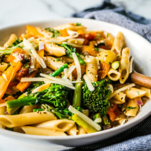 White serving bowl full of pasta primavera with a wooden serving spoon.