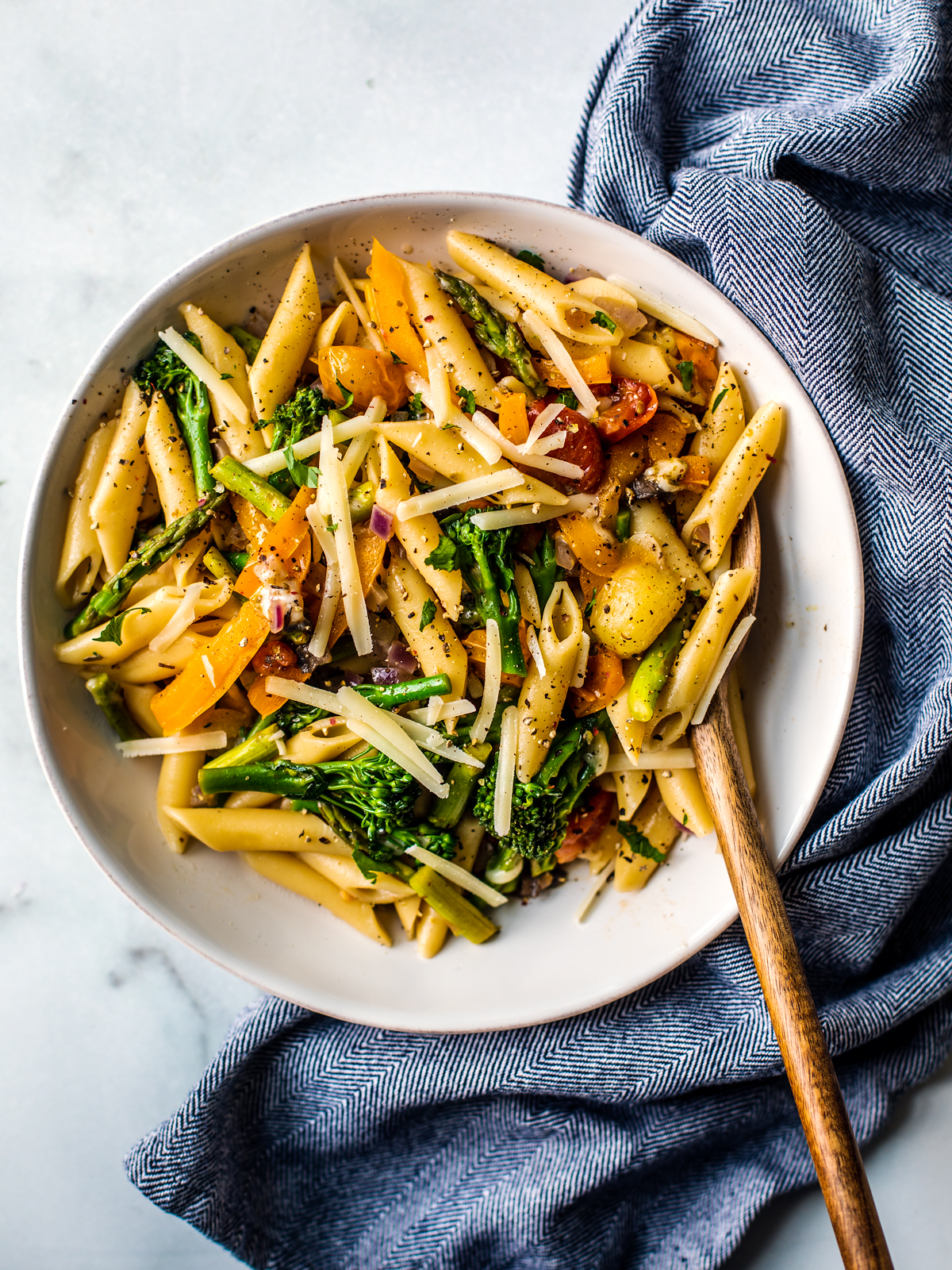 White serving bowl full of pasta primavera with a wooden serving spoon.