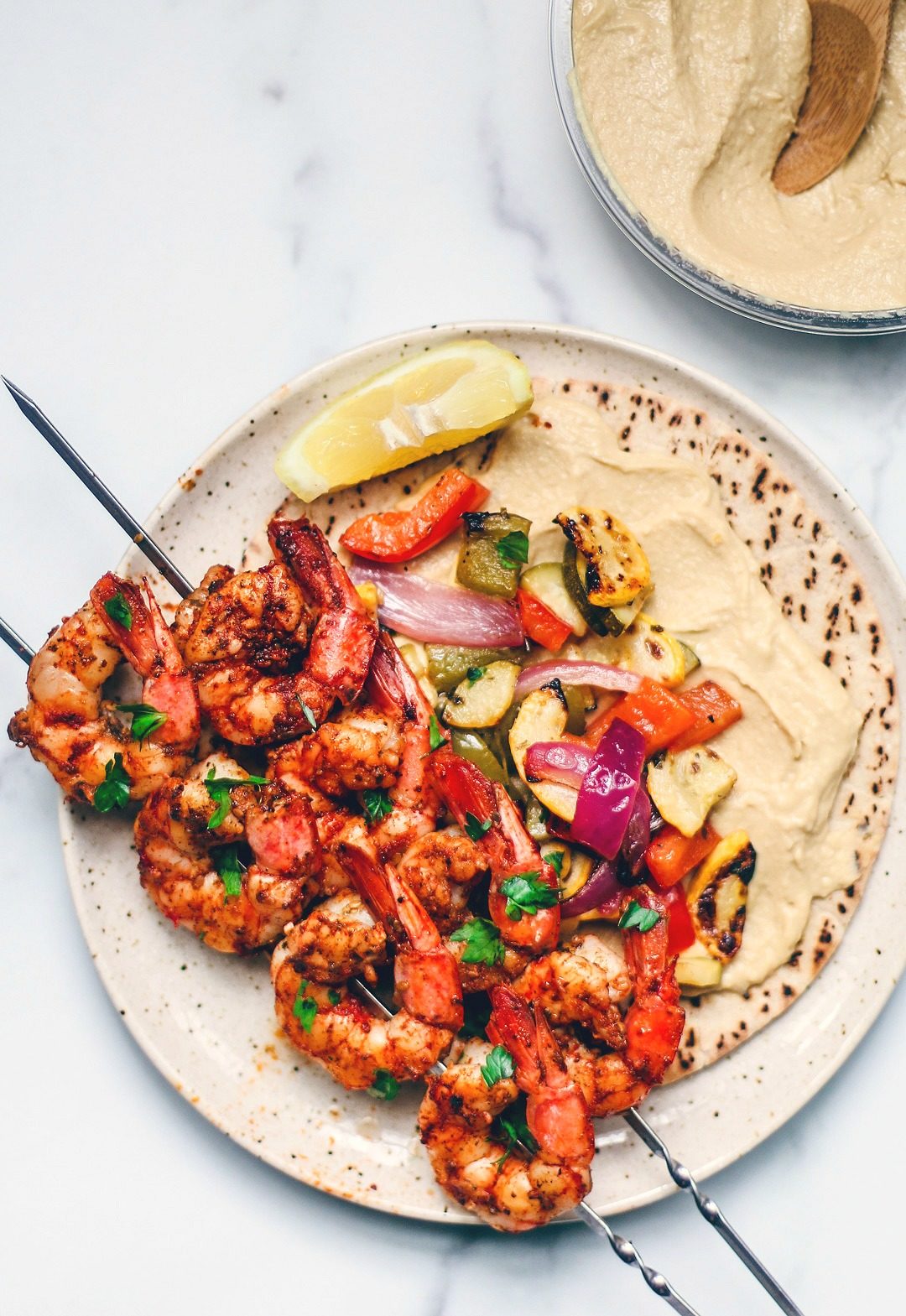 Grilled shrimp on a plate with veggies, pita, and hummus.