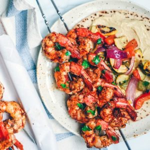 Grilled shrimp on a plate with veggies, pita, and hummus.