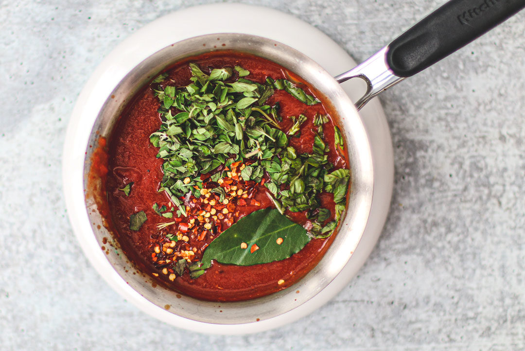 Sauce pot of marinara garnished with fresh herbs and pepper flakes.