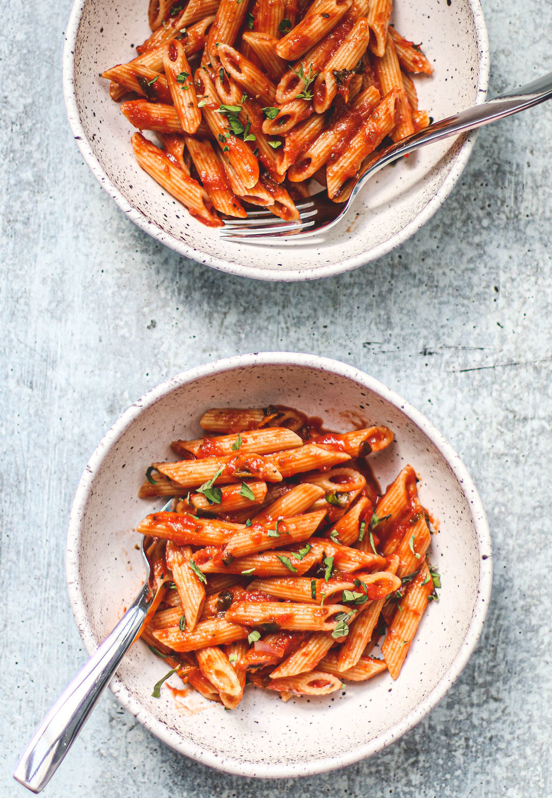 Two bowls of penne tossed in marinara.