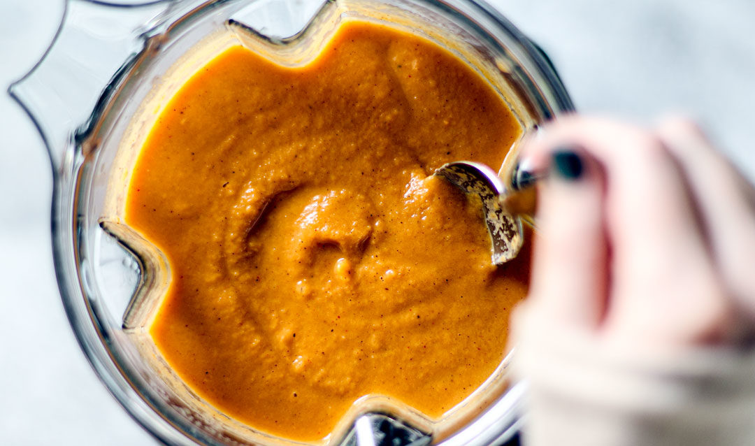 Close up of hand stirring blended sweet potato soup in blender.