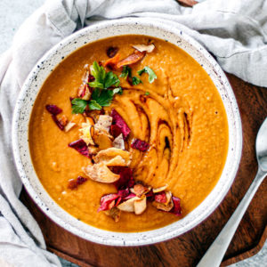 Bowl of sweet potato soup with colorful root chips and green herbs scattered over the top.