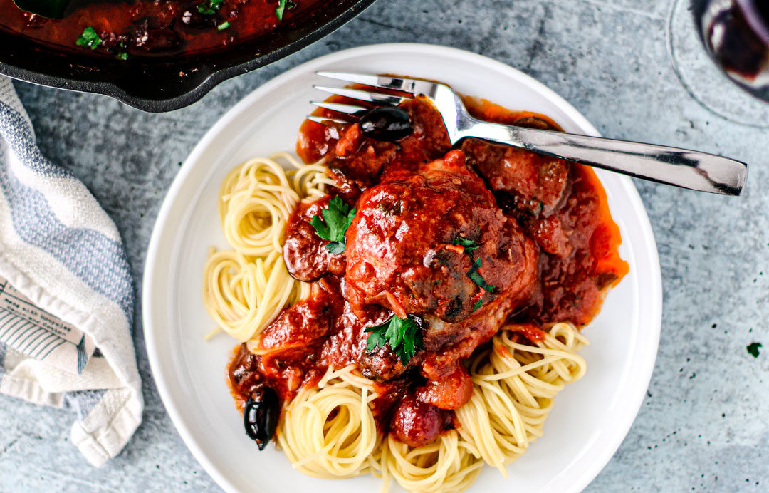 Plate of spaghetti topped with saucy chicken cacciatore.