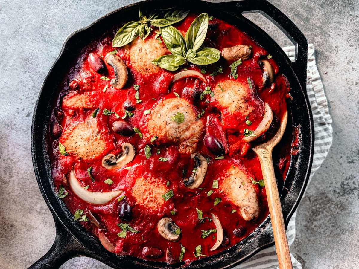 Chicken cacciatore in a skillet garnished with fresh basil. 