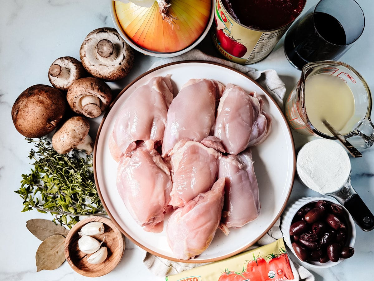 Ingredients for chicken cacciatore on a white marble background.
